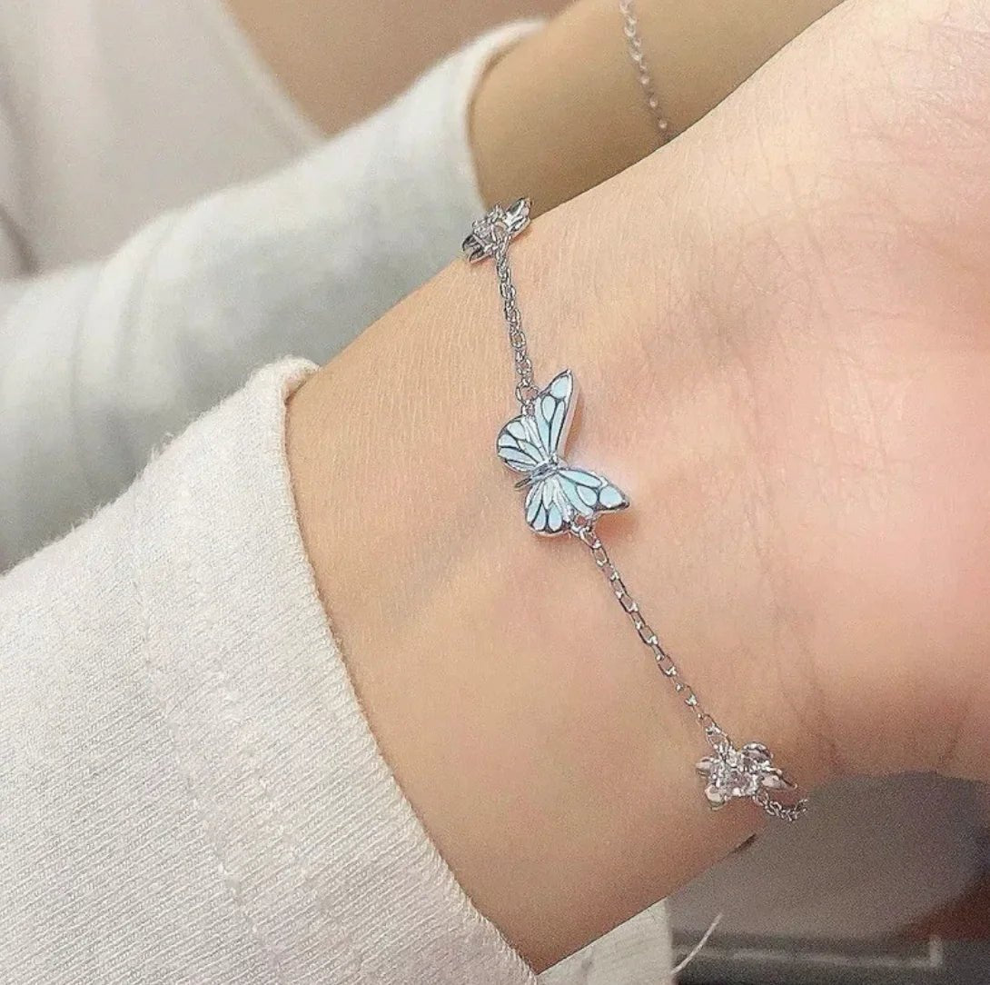 a hand showing a glow-in-the-dark butterfly pendant bracelet made of titanium steel with a white and blue color scheme.