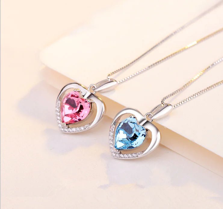 Two heart-shaped crystal pendants necklaces on a silver chain, one pink and one blue.