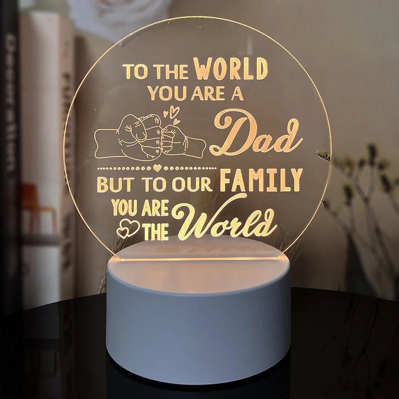An engraved acrylic night light with a message 'To the world you are a Dad, but to our family you are the world' in cursive and heart illustrations.