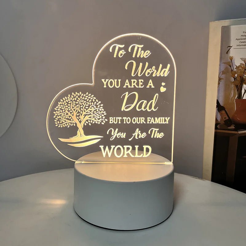 An engraved acrylic night light with a message 'To the world you are a Dad, but to our family you are the world' in cursive and heart illustrations.