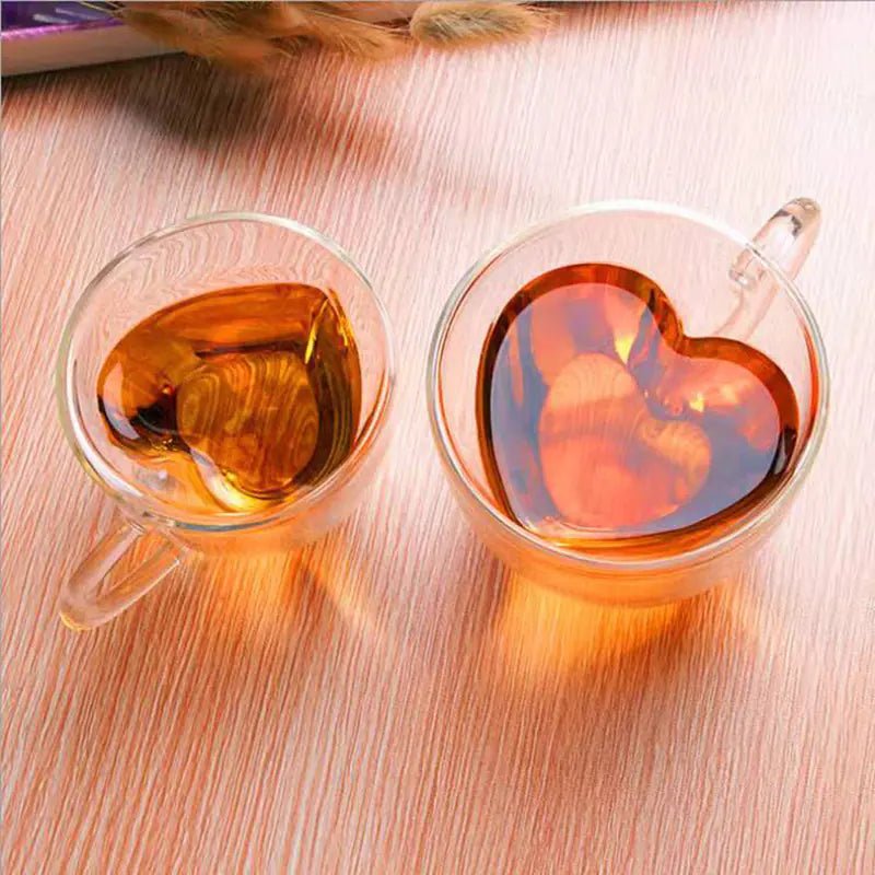 Two clear glass mugs with heart-shaped interiors with orange beverage