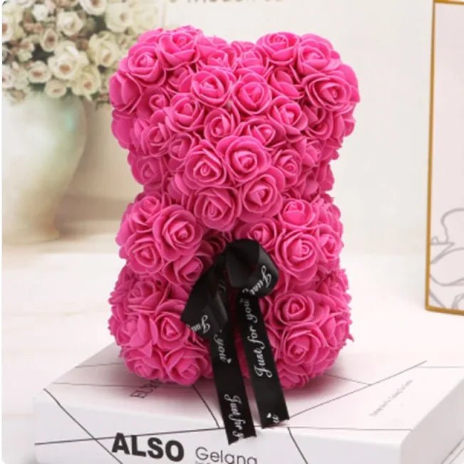 A teddy bear made from Dark pink artifical roses, with a black ribbon bow.