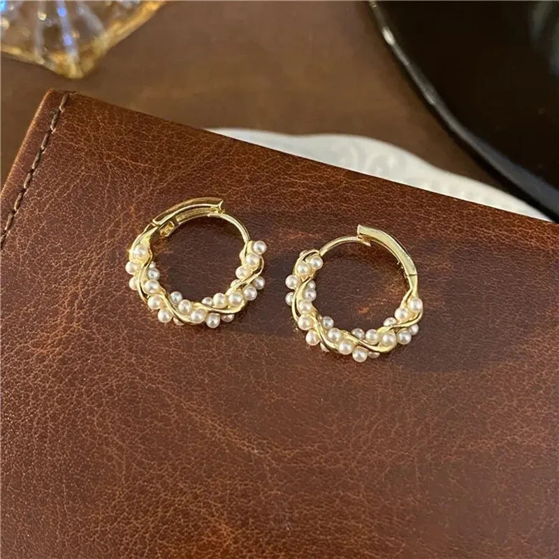 Gold hoop earrings with pearls on a brown leather surface