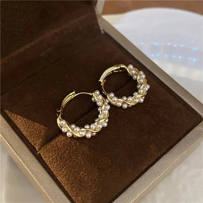 Gold hoop earrings with pearls on a brown velvet surface inside an open jewelry box.