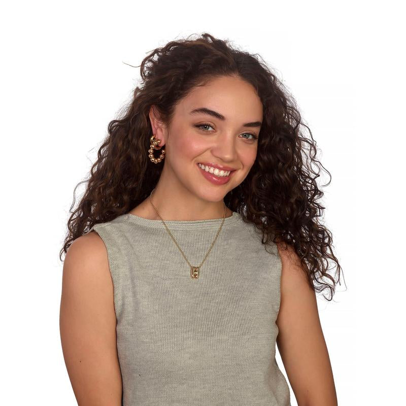 Woman with curly hair wearing a gray sleeveless top and gold jewelry