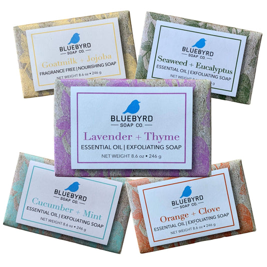 A set of five exfoliating soap bars with various labels indicating the scent and properties of each bar, such as Lavender Thyme, Cucumber Mint, and Orange Clove.