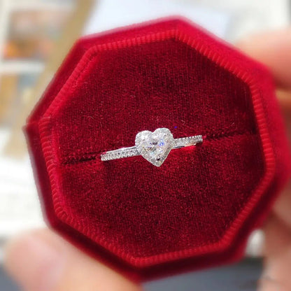 A sterling silver heart-shaped ring with a platinum-colored finish, displayed on a red octagonal cushion.