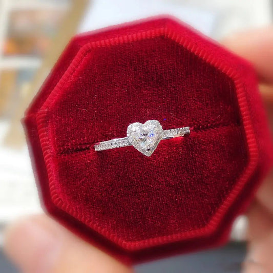 A sterling silver heart-shaped ring with a platinum-colored finish, displayed on a red octagonal cushion.