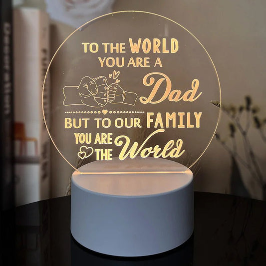 An engraved acrylic night light with a message 'To the world you are a Dad, but to our family you are the world' in cursive and heart illustrations.